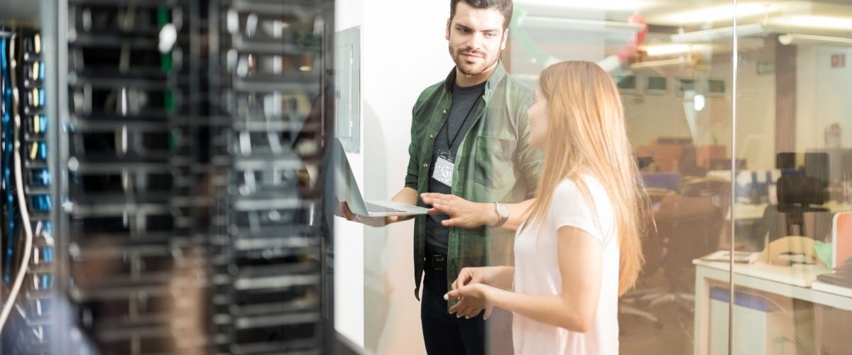 Two business people standing in server room with laptop and discussing